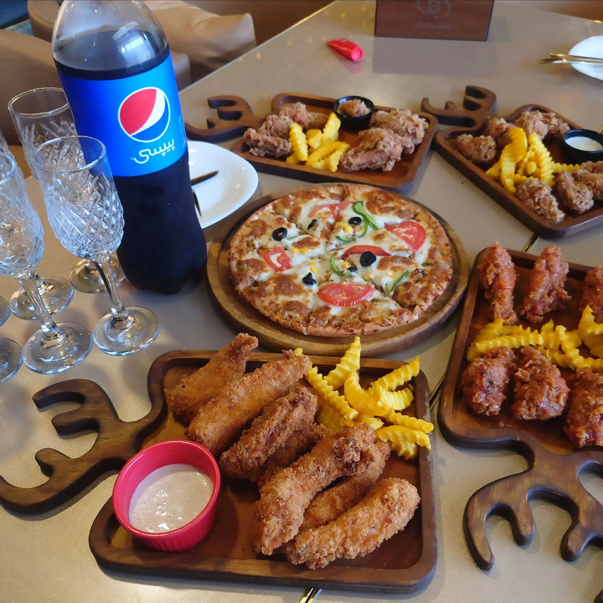 A shared Belal Pizza table with pizza, fried chicken platters, fries, sauces and cold drinks